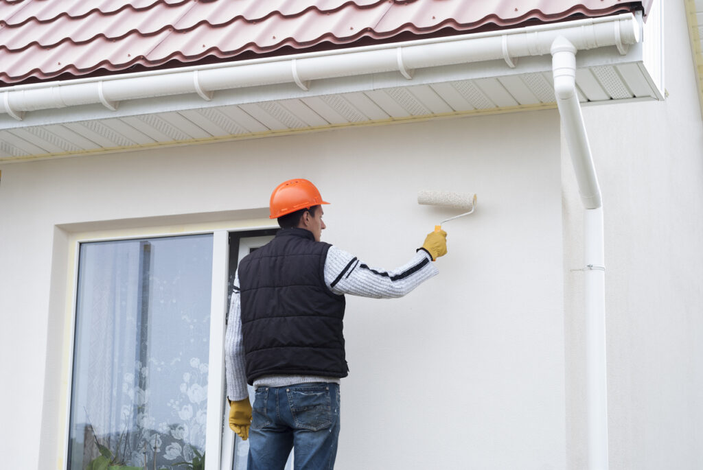 Homme équipé qui peint la façade de sa maison en blanc